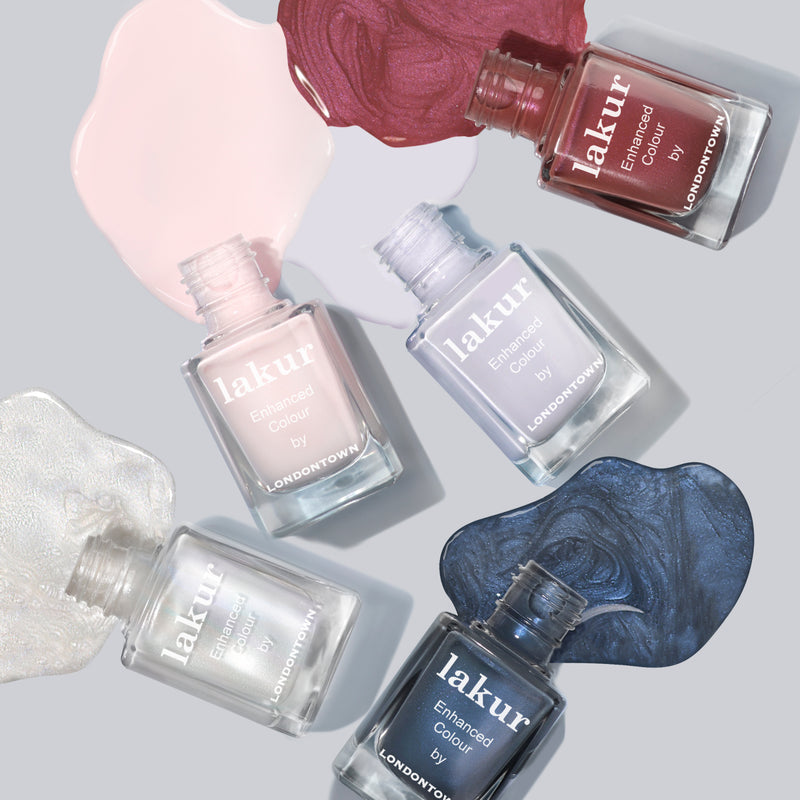 Five bottles of LONDONTOWN's Frostbitten nail polish in a variety of colors are displayed with open caps, and the corresponding polish is spread near each. The shades include various hues of pink, red, gray, and a cool ice blue.