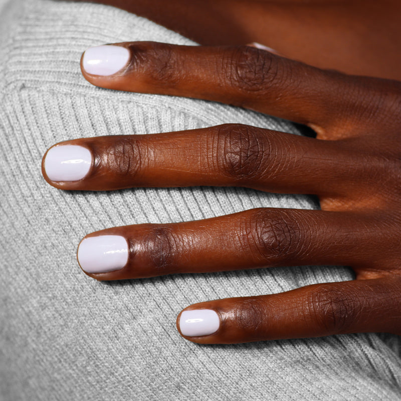 A person with neatly manicured fingernails painted in Frostbitten by LONDONTOWN rests their hand on their shoulder, showcasing a contrasting soft grey knit fabric with a subtle hint of ice blue.