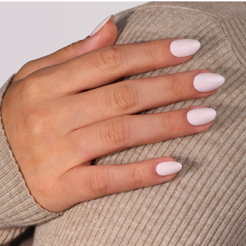 A hand with neatly manicured, short, almond-shaped nails painted in LONDONTOWN's Ski Bunny rests on ribbed beige fabric, looking as delicate as pink-tinted cream.