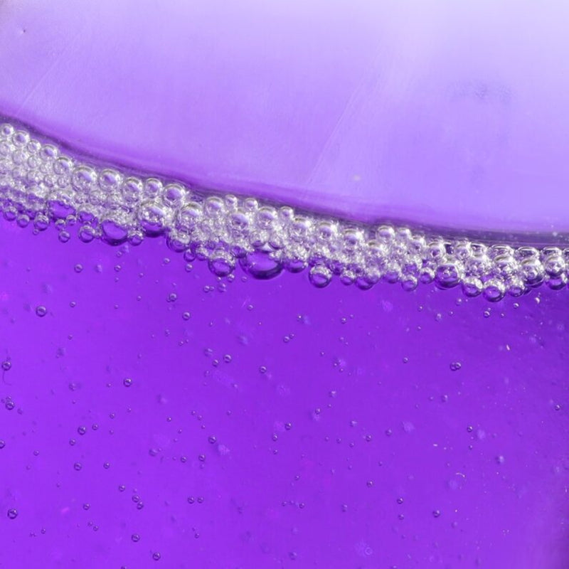 A close-up of the Nighttime Cuticle Quench - Lavender by LONDONTOWN reveals a purple liquid with numerous small bubbles forming a foamy layer along the surface, ideal for soothing cuticle treatment.