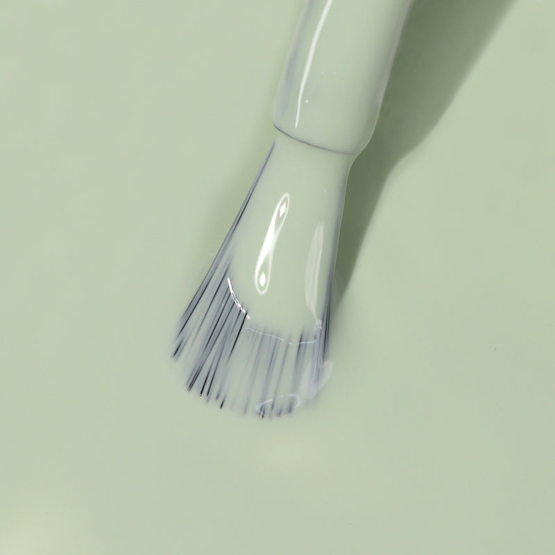 A close-up of a LONDONTOWN nail polish brush applying the pale green gel polish named Lichen, reminiscent of delicate white sage leaves.