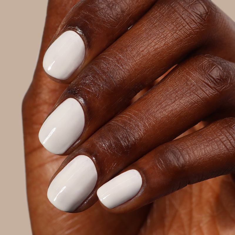 Close-up of a hand with dark skin and neatly manicured nails painted in LONDONTOWN's crisp, glossy white polish, "London Fog," reminiscent of cool clouds.