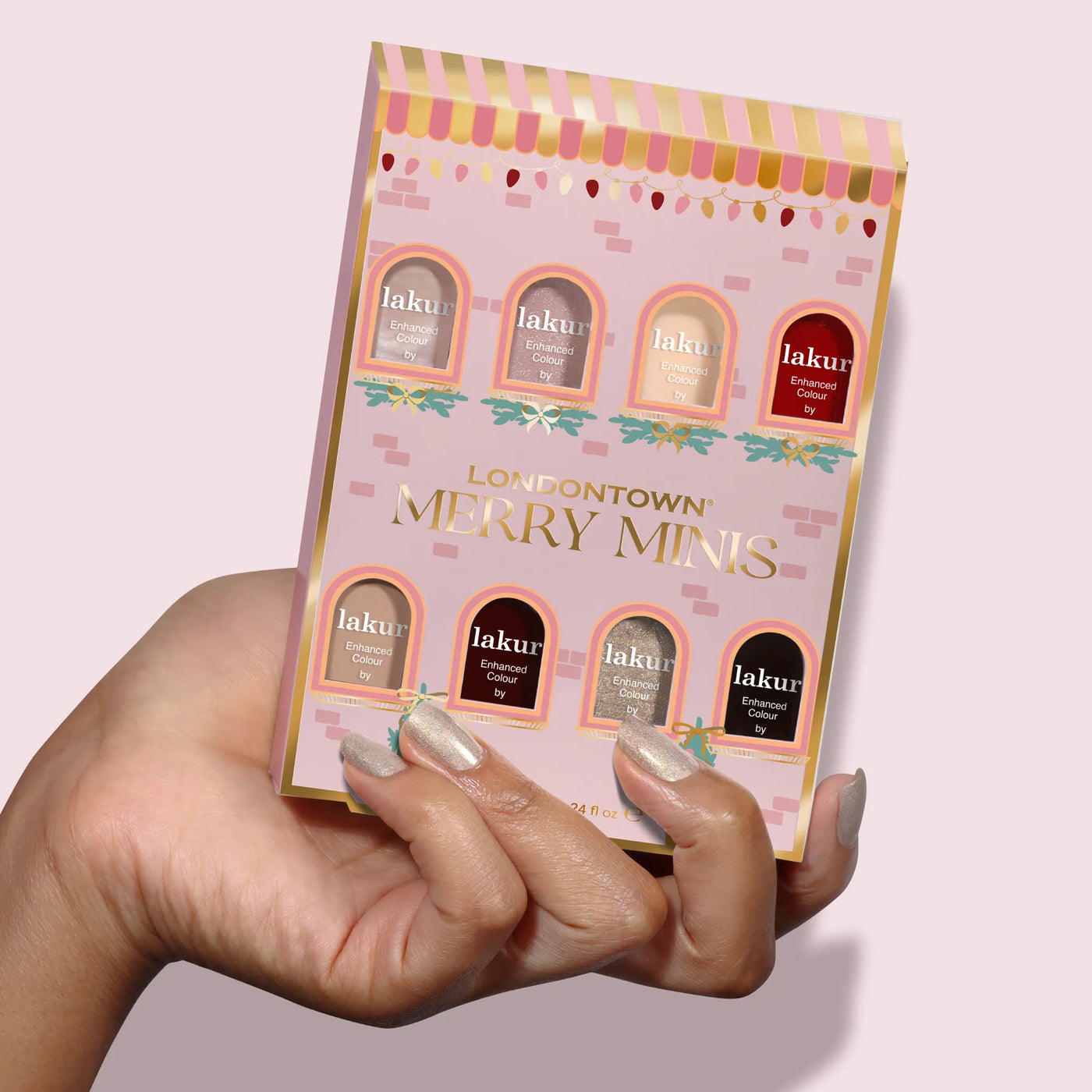 A hand holds the LONDONTOWN Merry Minis Set, featuring six assorted mini nail polishes in festive shades, all packaged in a cheerful pink and gold holiday box—perfect for seasonal manicures.