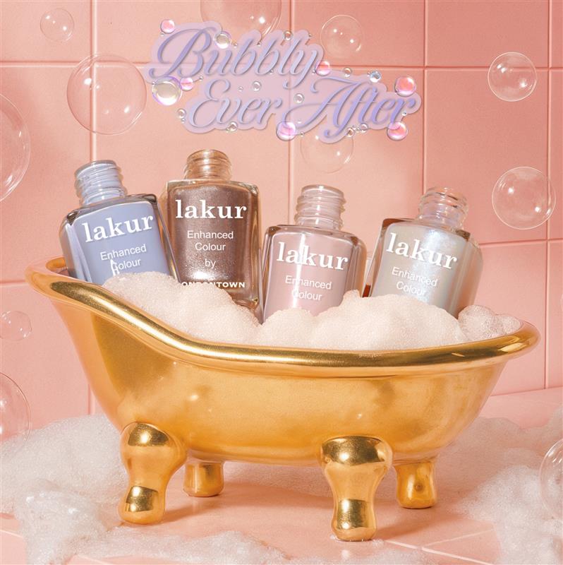 Four bottles of LONDONTOWN’s Milk Bath nail polish, in dreamy demi-sheer cream shades, rest in a gold mini bathtub filled with bubbles, set against pink tiles with “Bubbly Ever After” above.