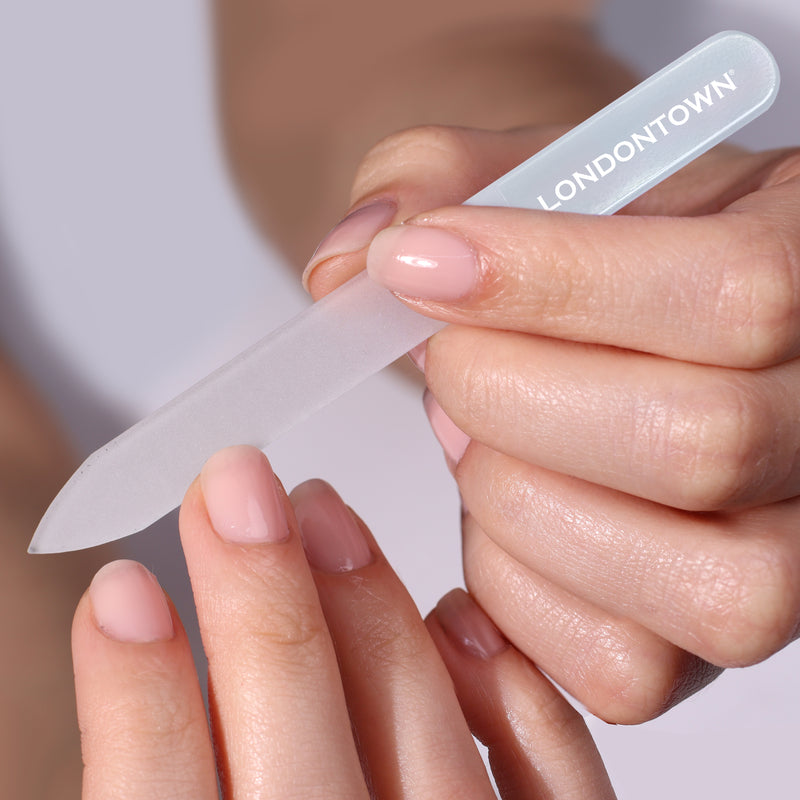 Close-up of a person effortlessly filing their nails with the "Glass Nail File - Milky" from LONDONTOWN. The nails, adorned with light pink polish, enjoy damage-free perfection.