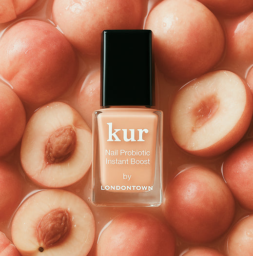 A bottle of LONDONTOWN Nail Probiotic Instant Boost, ideal for thin nails, sits on a surface with halved peaches in liquid.