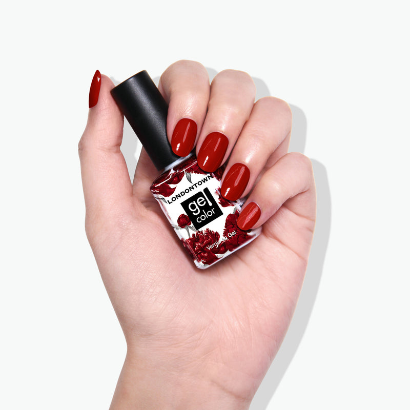 A hand holding a bottle of LONDONTOWN's Mull It Over gel nail color showcases burgundy painted nails, offering a decadent and sophisticated look.