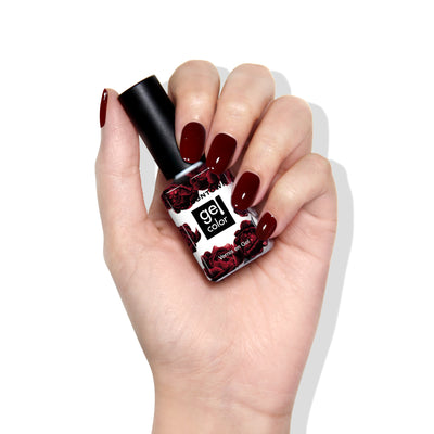 A hand with dark red Naughty List gel nail polish by LONDONTOWN holds a matching bottle featuring a floral label design against a white background.