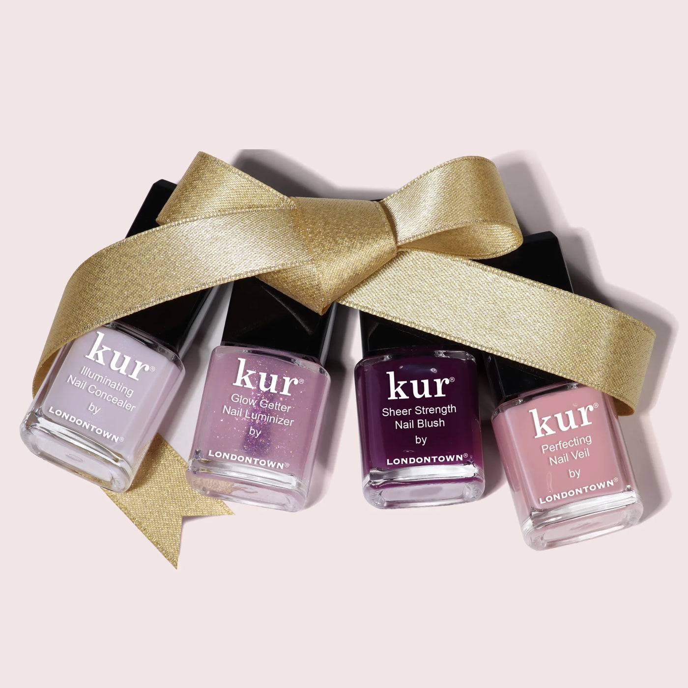 Four bottles of LONDONTOWN's One-Step Hero Minis are lined up with a gold ribbon bow, offering vibrant shades and nail care in one for a polished, elegant look.