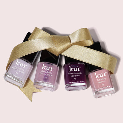 Four bottles of LONDONTOWN's One-Step Hero Minis are lined up with a gold ribbon bow, offering vibrant shades and nail care in one for a polished, elegant look.