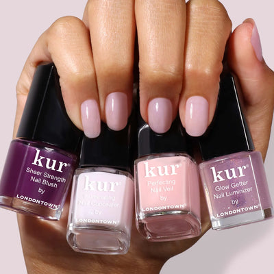 A hand with manicured nails holds four bottles of LONDONTOWN One-Step Hero Minis in assorted pink and purple shades, combining color and care for a flawless finish.