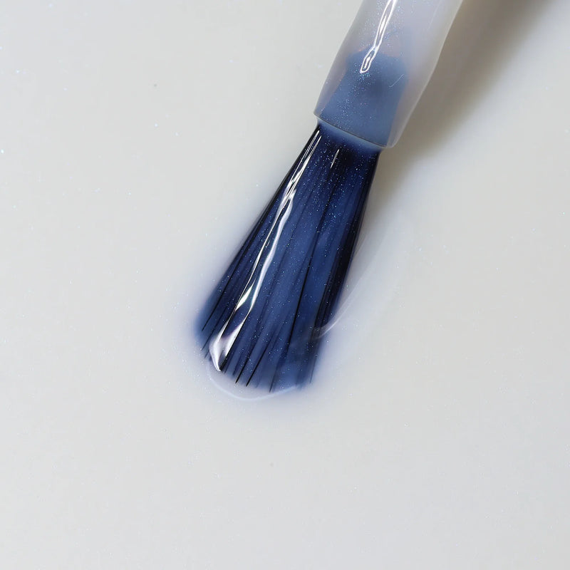 A close-up of a nail polish brush applying LONDONTOWN Original Illuminating Nail Concealer onto dull nails on a white surface.