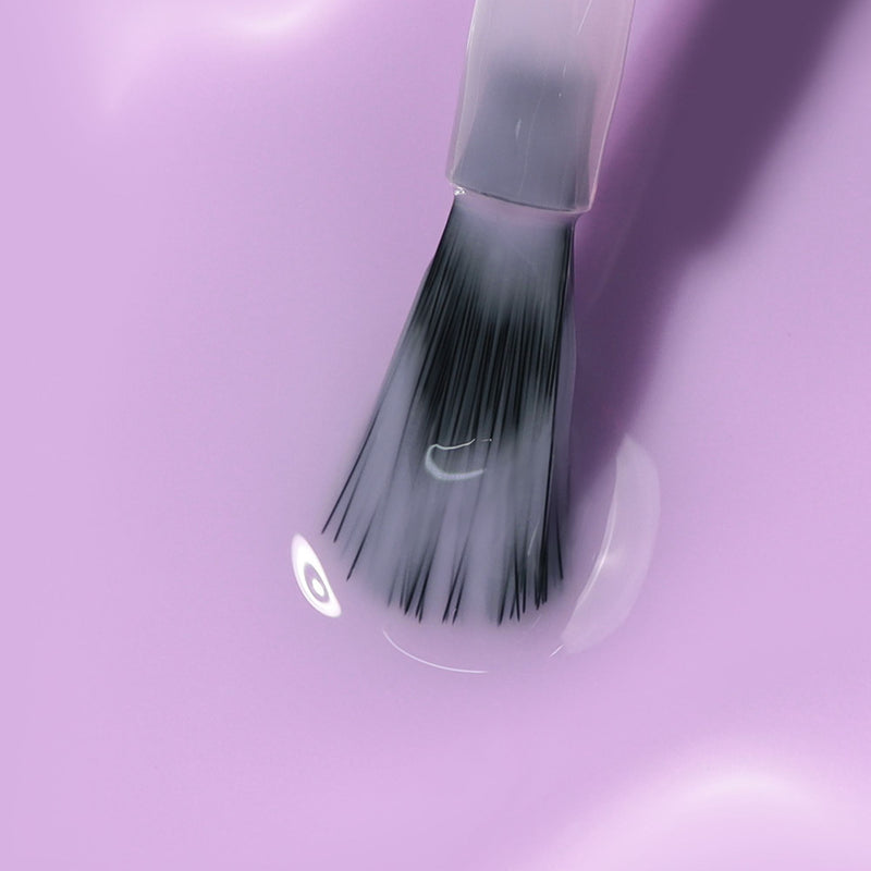A brush with a clear handle dips into the power-packed, glossy light purple liquid of LONDONTOWN's Perfecting Nail Veil #9, giving just a hint of color.