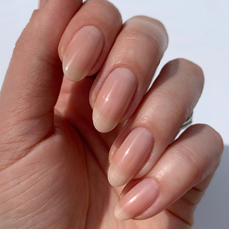 Close-up of a hand with natural, well-groomed, oval nails enhanced by LONDONTOWN Perfecting Nail Veil #4, showing a hint of color and care against a plain background.