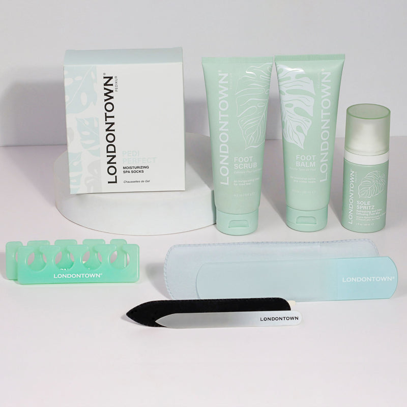 Introducing the Pedi Discovery Set by LONDONTOWN, a luxurious pedicure collection featuring foot care favorites: Pedi Perfect Moisturizing Sock, Foot Scrub, Foot Balm, Sole Spritz, a toe separator, a nail file, and a foot file.