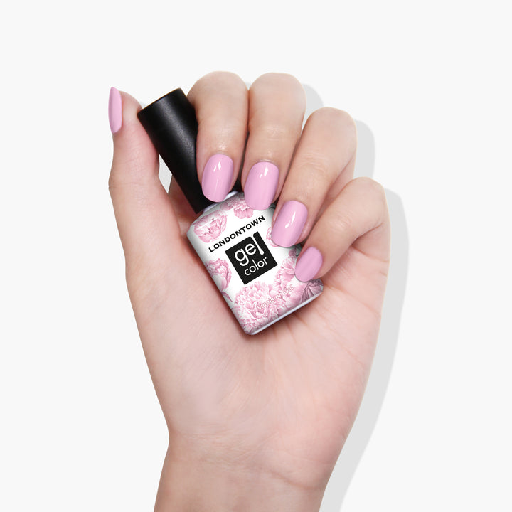 A hand with manicured nails painted a pastel shade of light pink holds a bottle of LONDONTOWN&