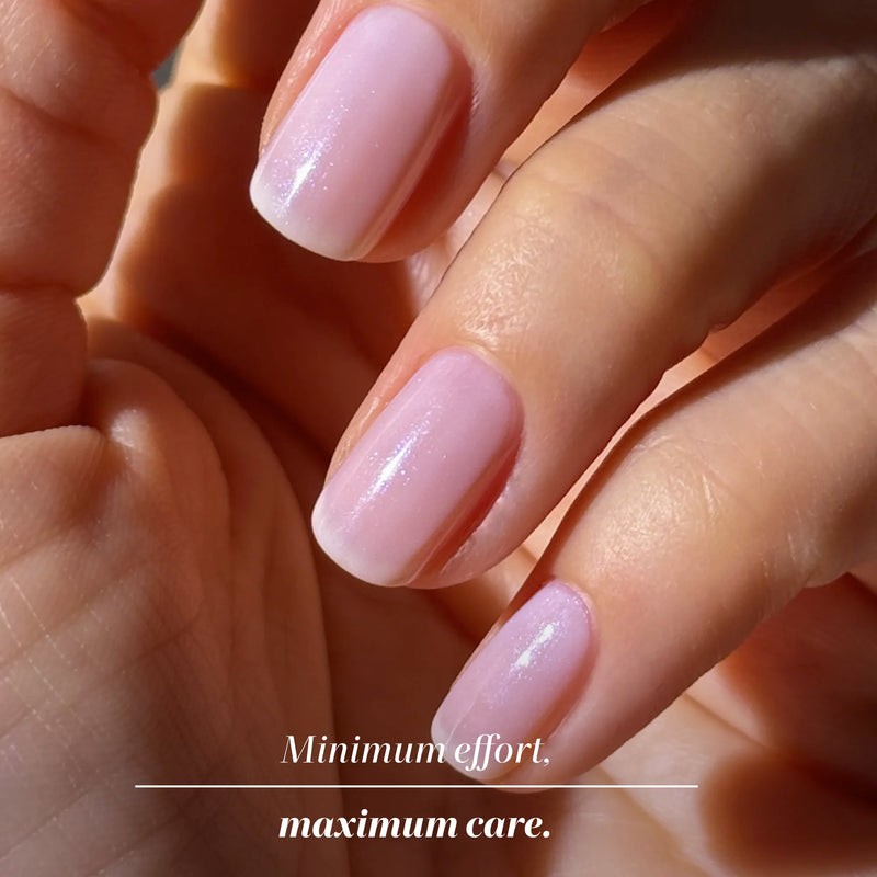 Close-up of a hand with neatly manicured, light pink nails in sunlight; text reads, "Minimum effort. Maximum care." Featuring LONDONTOWN Pink Illuminating Nail Concealer for a milky pink finish.