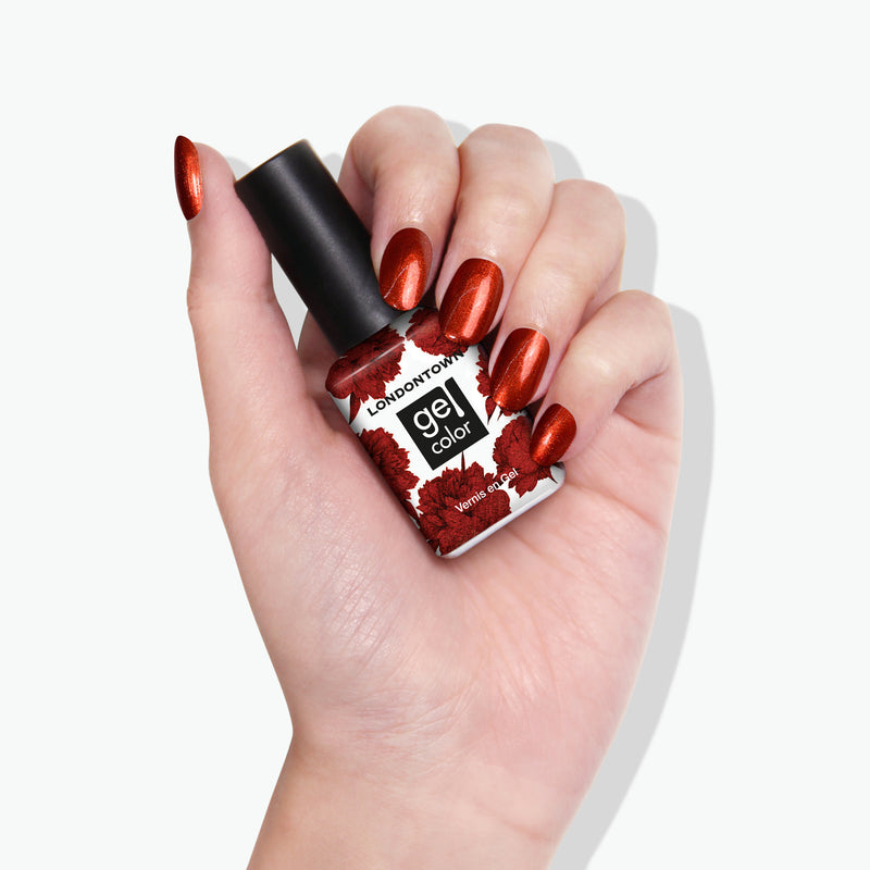 A hand holds a bottle of LONDONTOWN's "Posh Forever" gel nail polish, with metallic, cinnamon-colored nails perfectly matching the polish in the bottle.