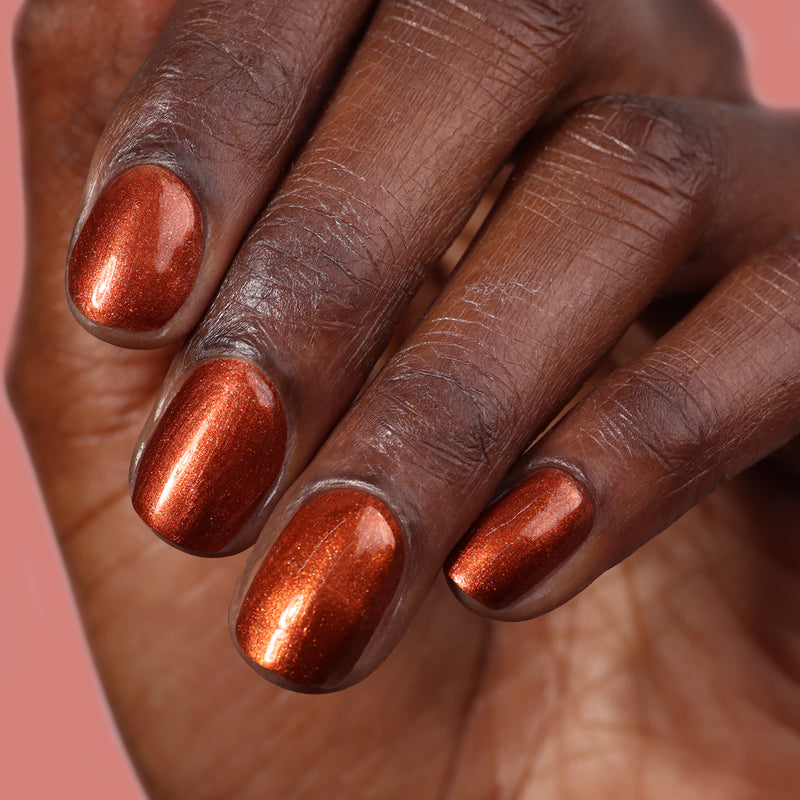 A close-up of a hand displaying short, neatly manicured nails painted with LONDONTOWN's Posh Forever metallic cinnamon copper nail polish.