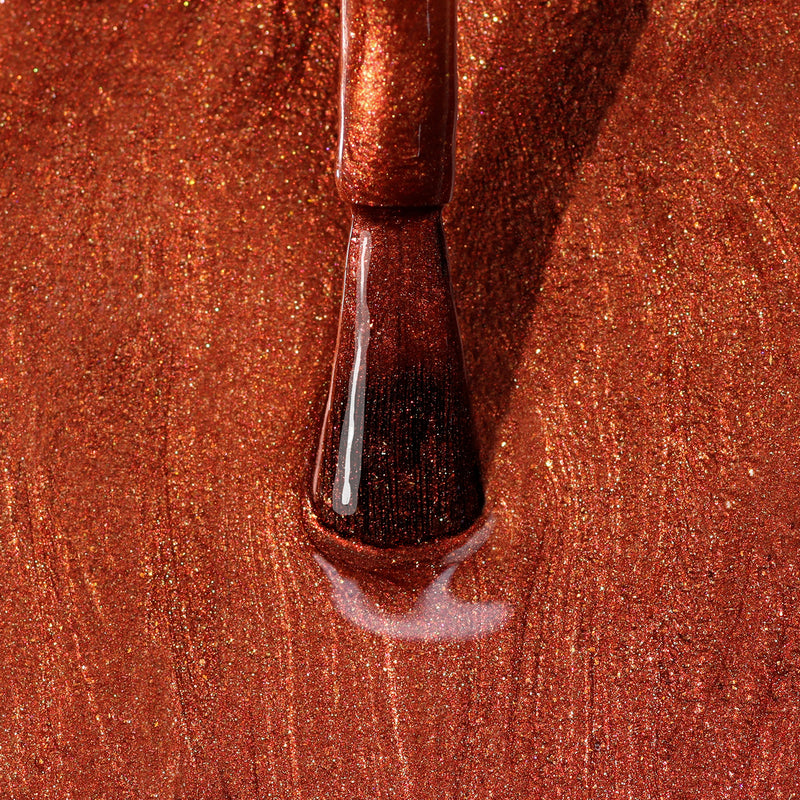 Close-up of a nail polish brush applying Posh Forever by LONDONTOWN, a cinnamon-toned metallic red nail polish with a shimmering effect.
