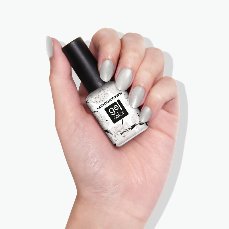 A hand with light gray, snow-inspired painted nails holding a bottle of LONDONTOWN Gel Color nail polish in the shade "Powder.