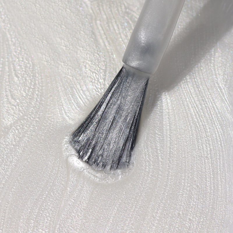 Close-up of a brush applying LONDONTOWN's Powder, a shiny, translucent liquid with a swirling texture on a surface, reminiscent of chrome.