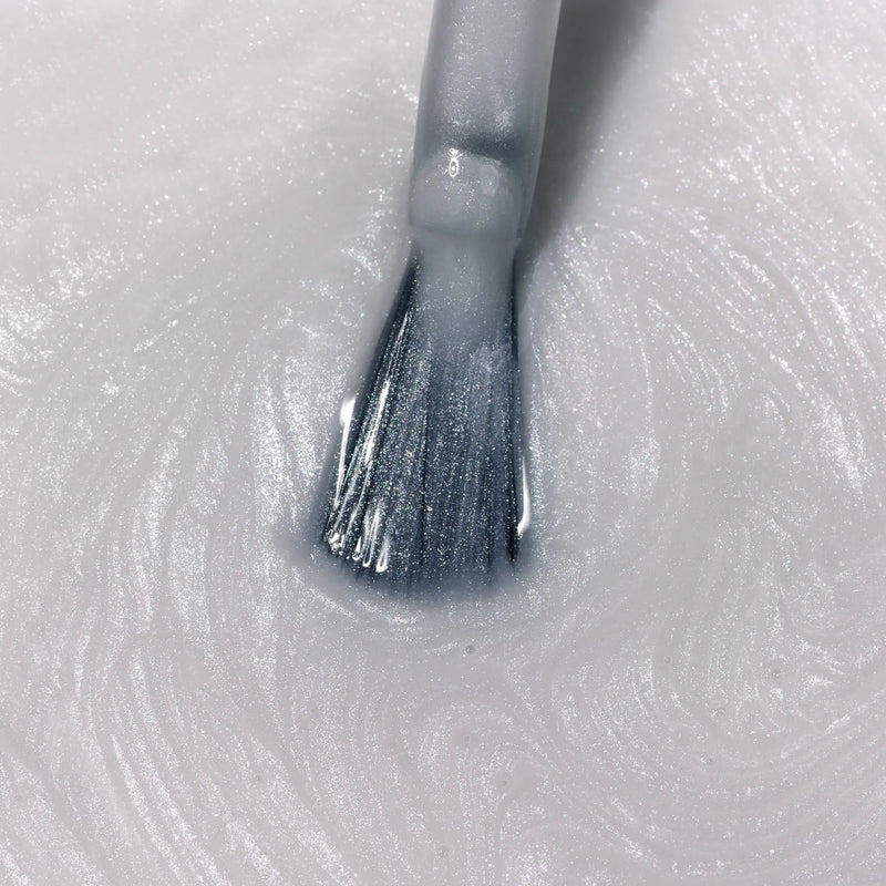 A close-up of the LONDONTOWN Quartz Illuminating Nail Concealer brush resting on a textured, shimmery white surface.