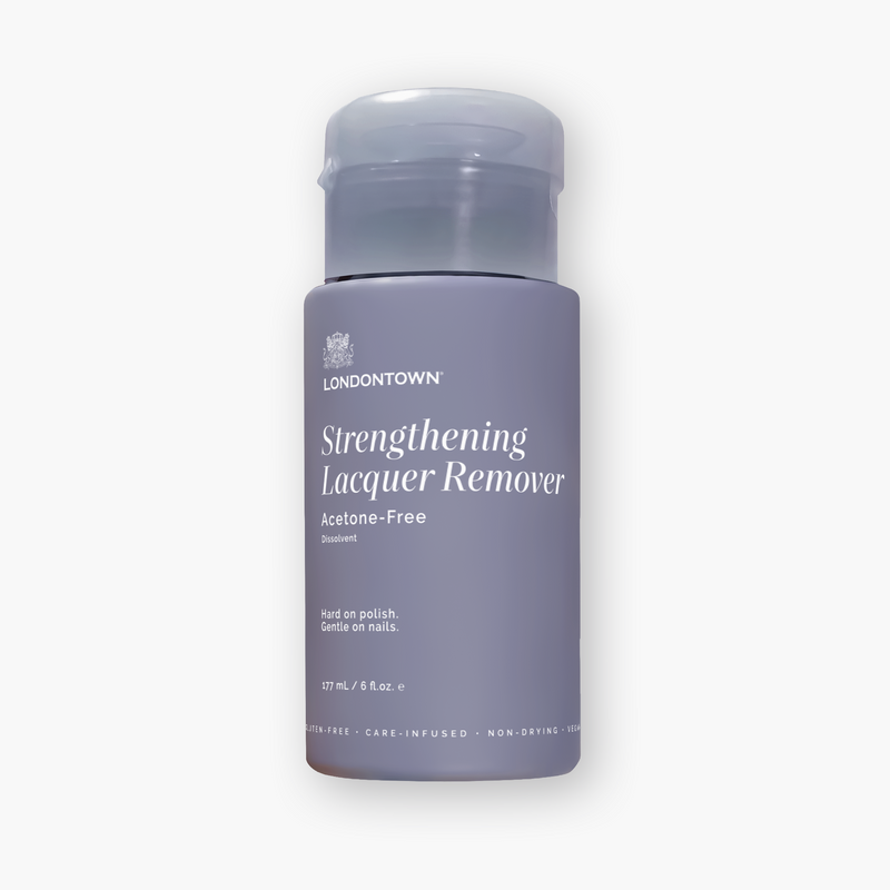 A 177 mL bottle of LONDONTOWN Strengthening Lacquer Remover, a moisturizing and gentle non-acetone nail polish remover with a gray-purple label and flip-top cap, designed for gentle nail polish removal.