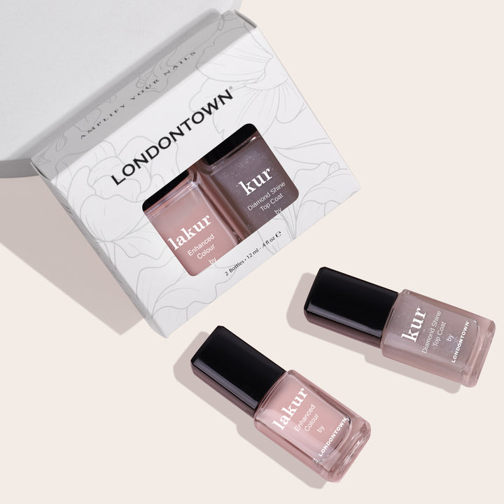 A box labeled "LONDONTOWN" containing the "Royal Manicure" set with two nail polish bottles is displayed. The two polishes, one labeled "lakur" and the other "kur," are placed outside the box on a light background, showcasing sheer sophistication.