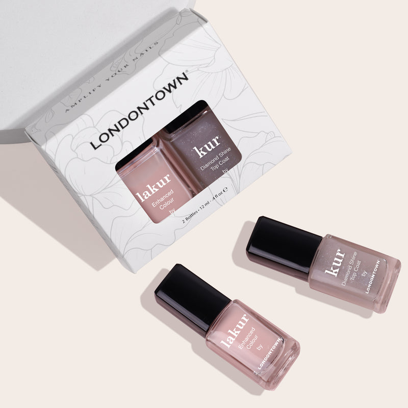 A box labeled "LONDONTOWN" containing the "Royal Manicure" set with two nail polish bottles is displayed. The two polishes, one labeled "lakur" and the other "kur," are placed outside the box on a light background, showcasing sheer sophistication.