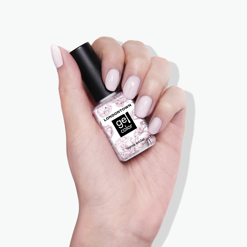 A hand with manicured light pink nails holds a bottle of LONDONTOWN's Ski Bunny gel color nail polish against a white background, perfectly complementing the pink-tinted cream finish.