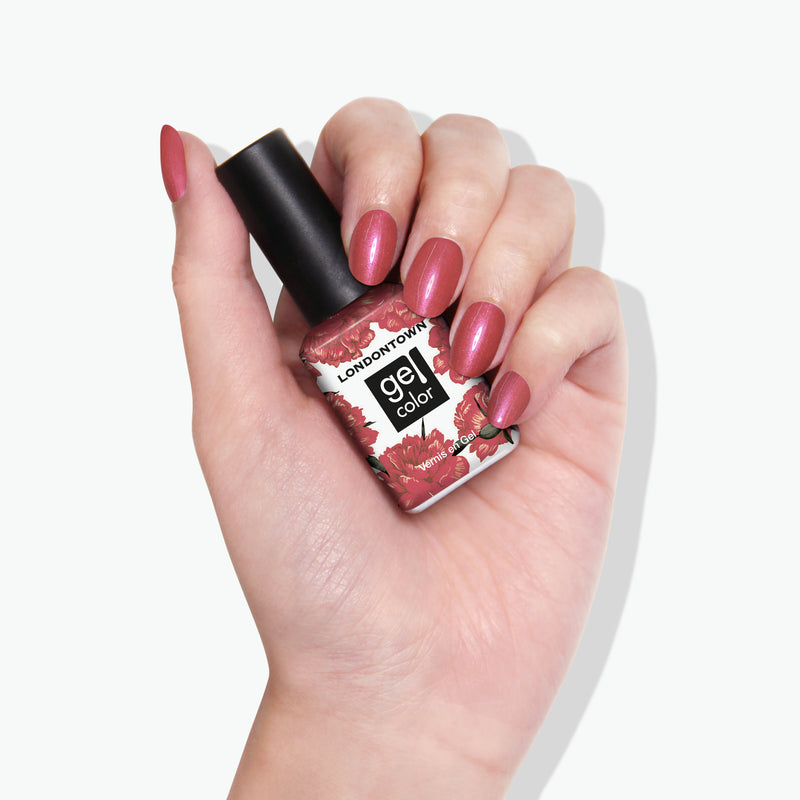 A hand holding a bottle of LONDONTOWN's Slopeside gel color nail polish. The nails, painted in a similar rose shade as the bottle's color, gleam with a subtle chrome finish.