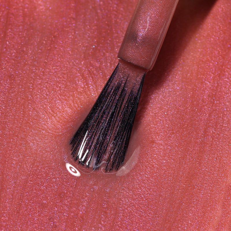 Close-up of a LONDONTOWN Slopeside nail polish brush applying rose-tinted, pinkish-gold polish with chrome shimmer on a textured surface.