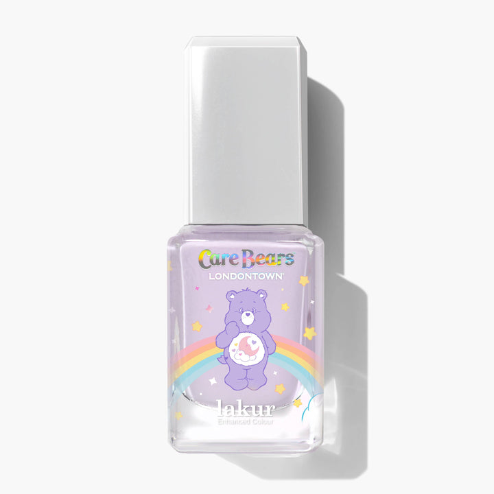 A bottle of LONDONTOWN Sweet Dreams Lakur nail polish features a Care Bears design with a lavender purple bear, rainbow, and stars on a light purple background for a soothing, comforting vibe.