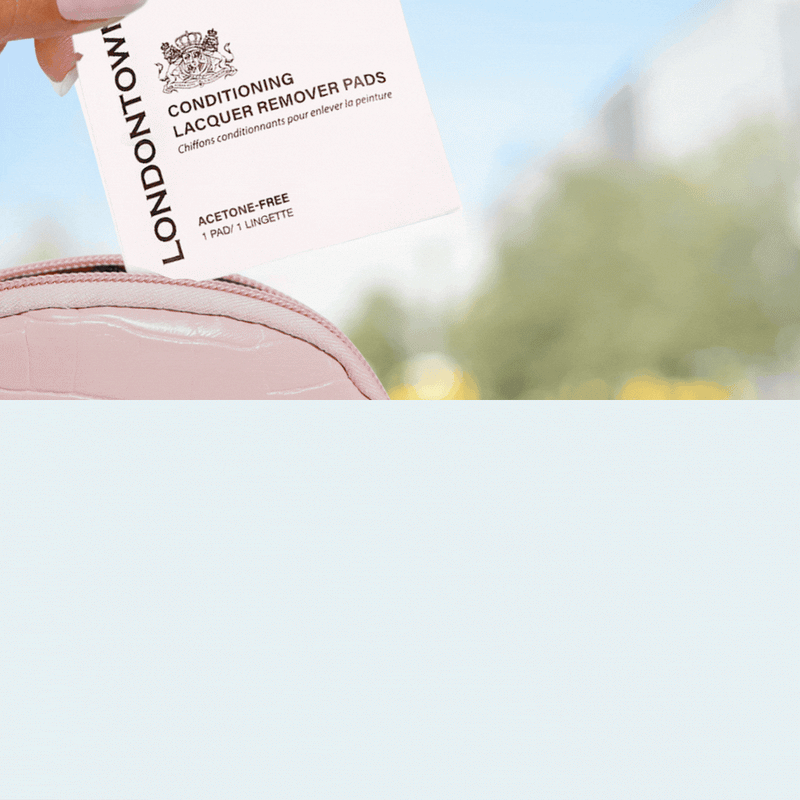 A hand displays a LONDONTOWN Home & Away Remover Set pad over a stylish pink bag, set against a gently blurred outdoor backdrop, embodying beauty and elegance.