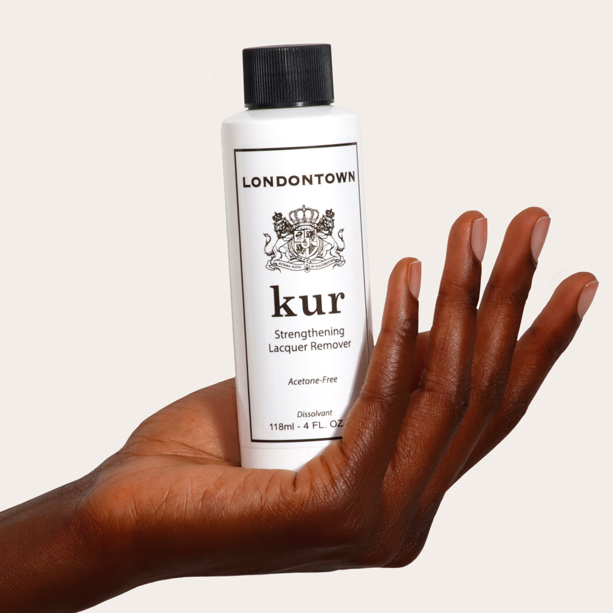 A hand holds a bottle of LONDONTOWN's Strengthening Lacquer Remover, 118ml, an acetone-free nail polish remover designed for vegan and cruelty-free nail care.