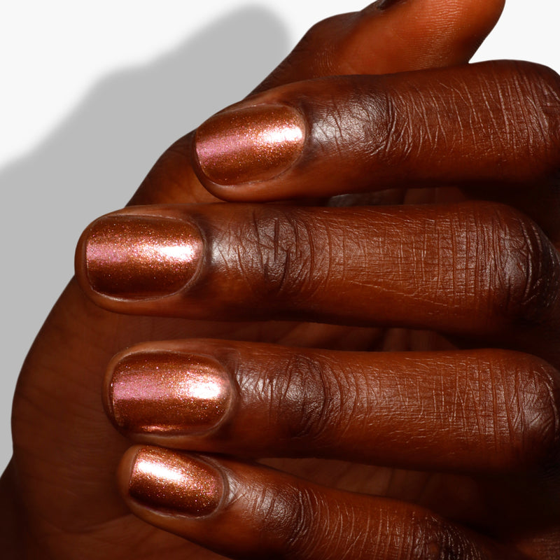 A close-up of a hand adorned with LONDONTOWN's The Runway Edit, a metallic rose gold nail polish, is featured on neatly trimmed nails against a white background.