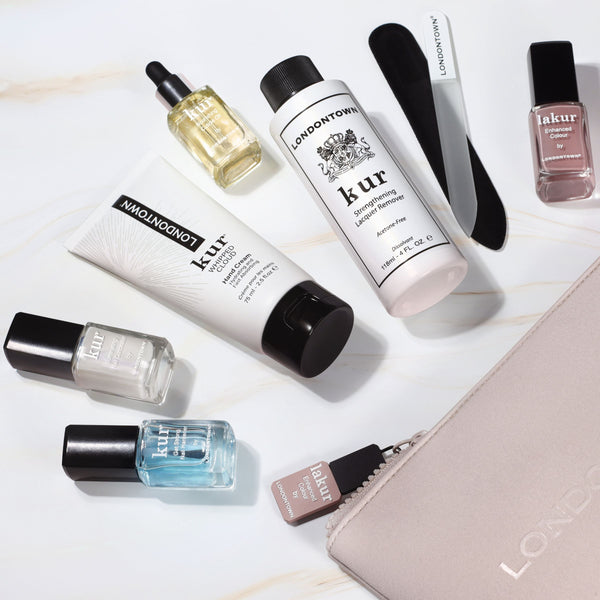 A neatly arranged collection of nail care products from the Londontown Discovery Set 2.0, featuring polishes, cuticle oil, nail files, and a chic cosmetic bag, graces the surface. This ensemble by LONDONTOWN hints at quality and style for your beauty regimen.