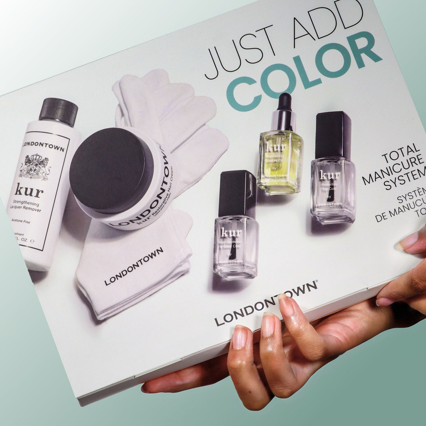 A person holds a boxed LONDONTOWN Just Add color manicure system, which includes nail care products, gloves, and bottles for an easy at-home manicure.