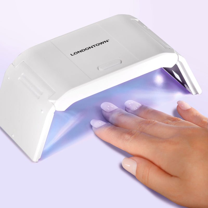A hand with painted nails is under the LONDONTOWN Foldable UV/LED Gel Lamp, which emits purple light to quickly cure gel polish and keep your manicure flawless on the go.