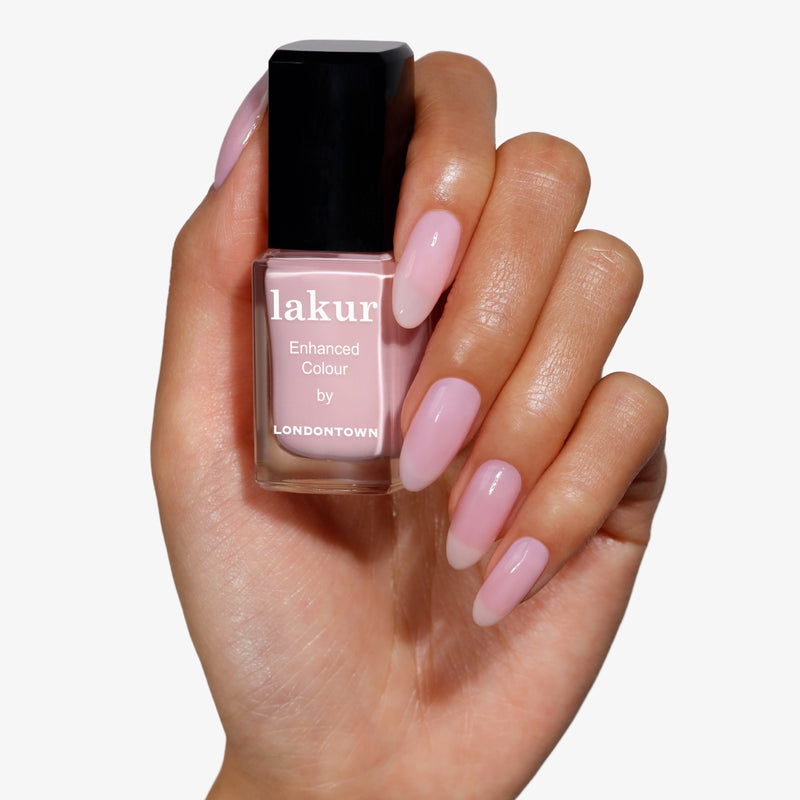 A hand holding a bottle of Magnolia Haze nail polish, a sheer, petal pink shade by LONDONTOWN.