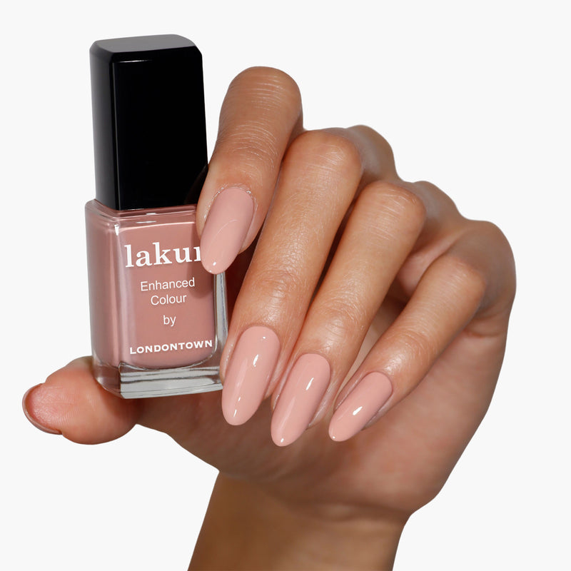 A hand with long, smooth nails painted in a glossy pink beige polish holds a bottle labeled "LONDONTOWN, Rose Latte.