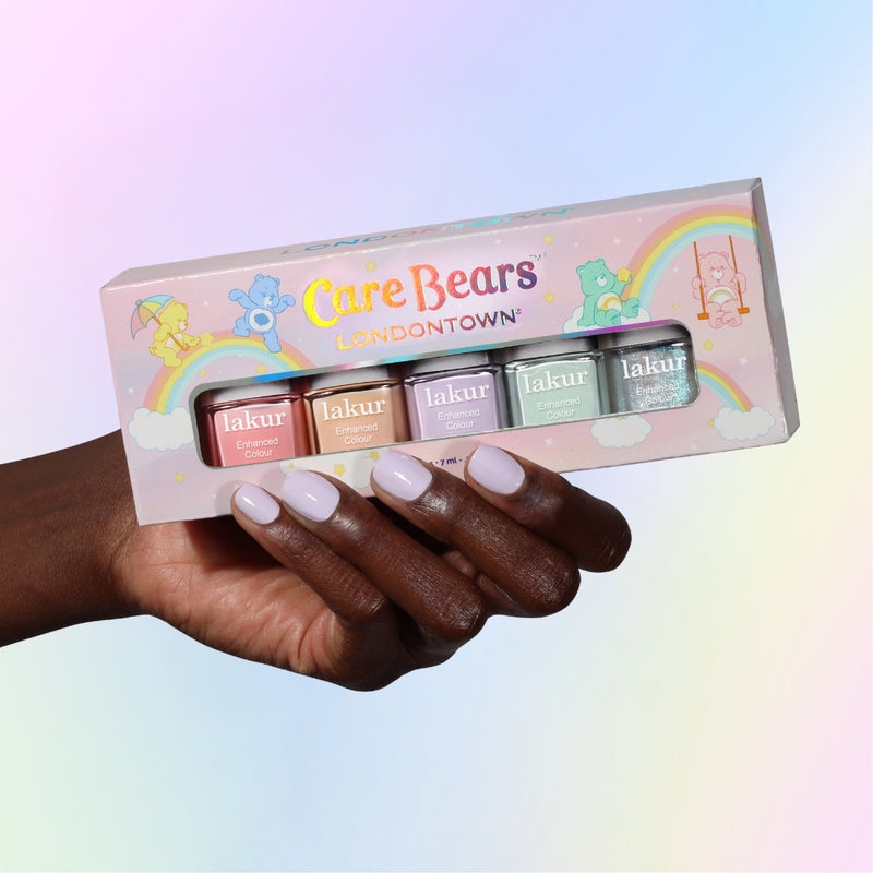 A hand with pale purple nails holds the LONDONTOWN Beary Polished Mini Set, featuring four pastel Care-A-Lot minis, against a pastel gradient background.