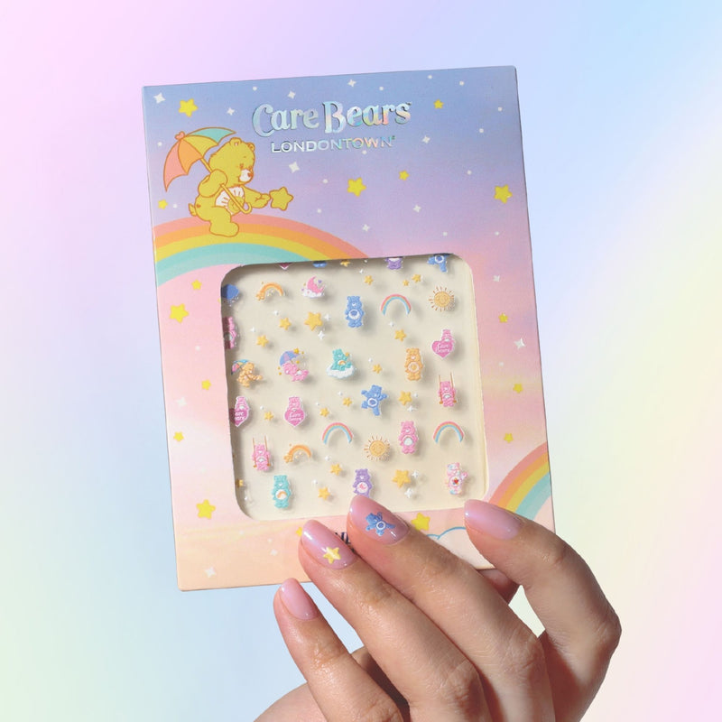 Hand holding a package of LONDONTOWN Care Bears Nail Decals featuring colorful bears, rainbows, and stars on a pastel gradient—perfect for easy nail art enthusiasts.