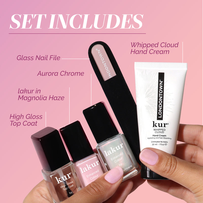 A hand holds LONDONTOWN’s Modern Chromance Valentine’s Day Set—glass nail file, Whipped Cloud hand cream, Aurora Chrome, Magnolia Haze polish, and pink glazed gloss top coat—capturing a love story of self-care on a pink background.