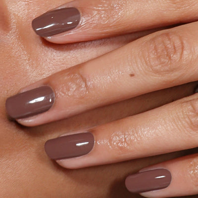 Close-up of a hand with neatly manicured nails painted in LONDONTOWN’s Dirty Chai, a glossy spiced brown taupe shade.