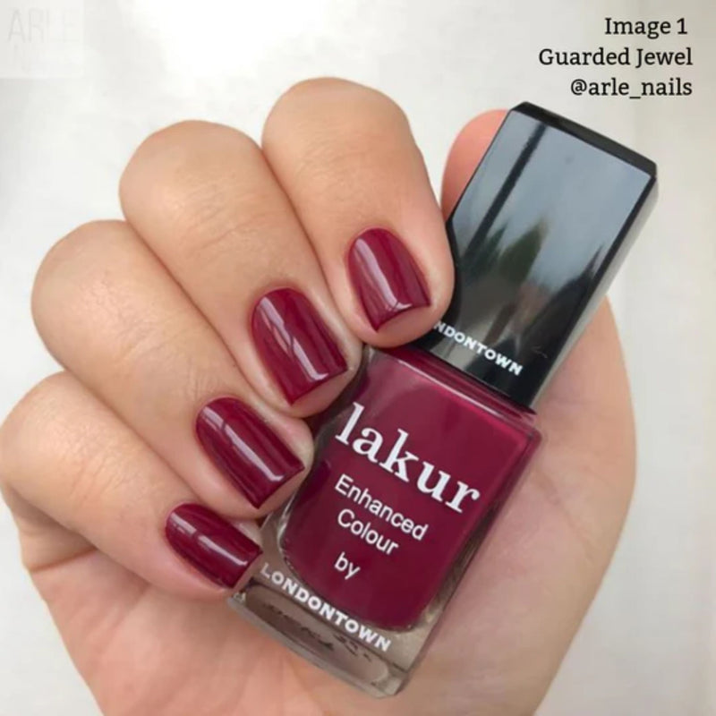 A manicured hand with deep red nails elegantly clutches LONDONTOWN's Guarded Jewel nail polish. This vegan, cruelty-free formula, enriched with Florium Complex, ensures brilliant shine.