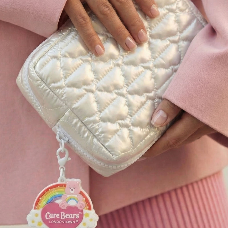 A person holds the Bear Necessities Set by LONDONTOWN—a quilted white keepsake pouch—while wearing a light pink coat and pleated pink skirt for a playful yet chic look.