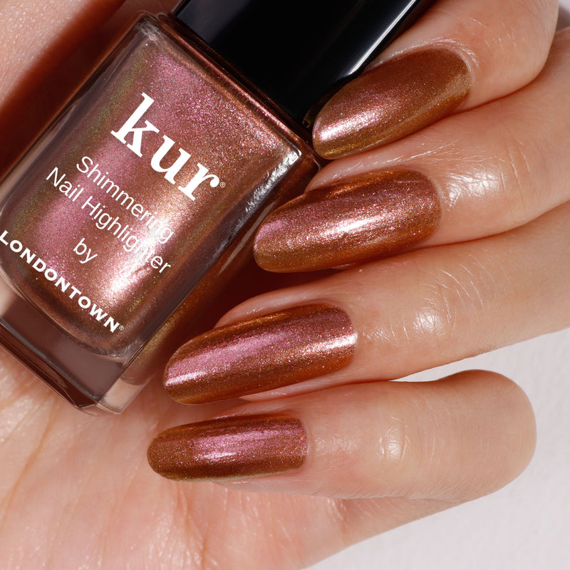 Close-up of a hand with long, shimmering bronze nails holding a nail polish bottle labeled "The Runway Edit" by LONDONTOWN.