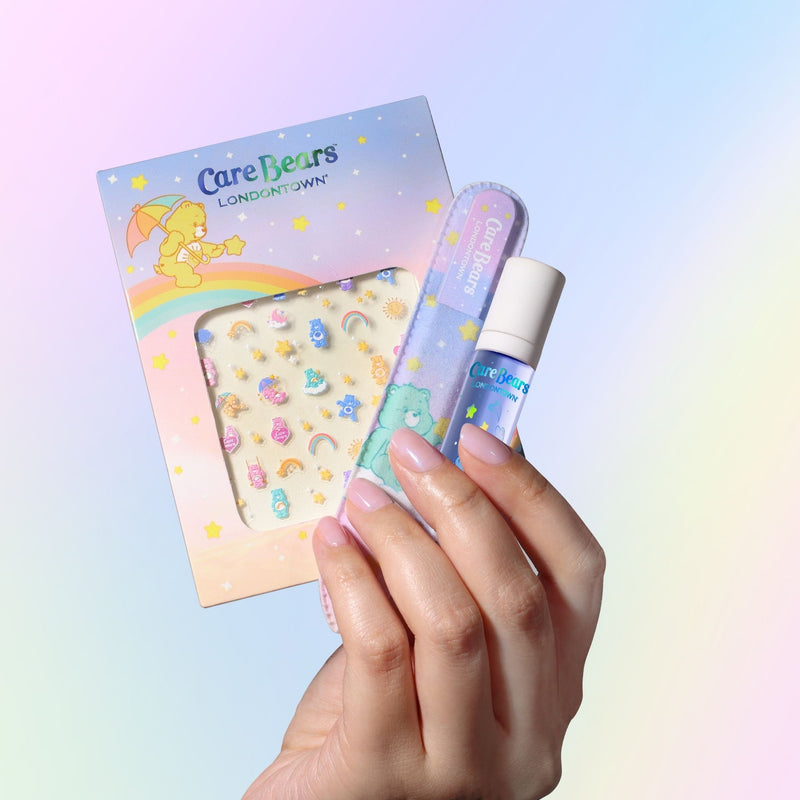 A hand displays LONDONTOWN's Bear Necessities Set: Care Bears-themed nail decals, a nail file, and pastel polish—all set against a soft gradient background and ideal for your keepsake pouch.